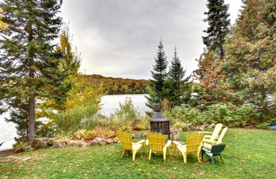 Cour aménagée avec foyer extérieur, chaises jaunes et le lac en arrière-plan
