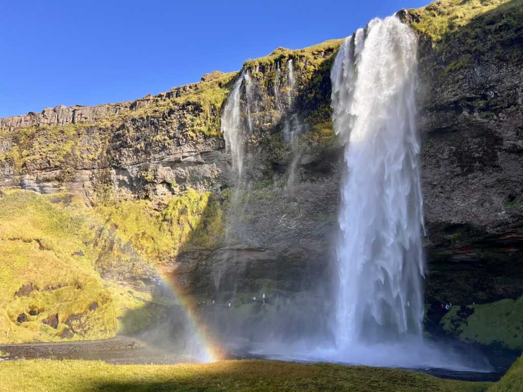 Puissante chute d’eau créant une brume naturelle et un arc-en-ciel, illustrant la présence élevée d’ions négatifs bénéfiques pour le bien-être lors d’un séjour en plein air.