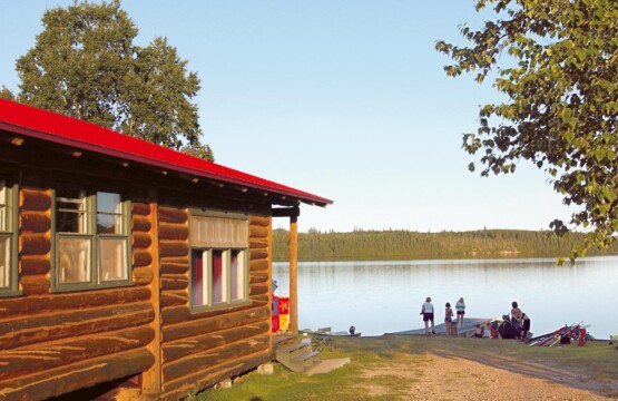 Petit chalet en bois rond avec une toiture rouge situé au bord de l'eau.