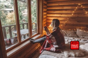 Femme qui se détend sur la galerie d’un chalet en bois rond.