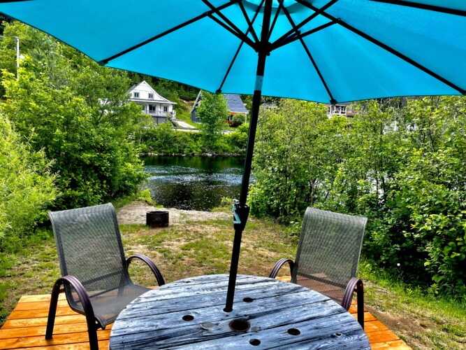 Petite table avec parasol bleu au bord de la rivière du Chalet à louer Chalet l’Ancestrale à Lanaudière, chalet avec spa à Saint-Côme.