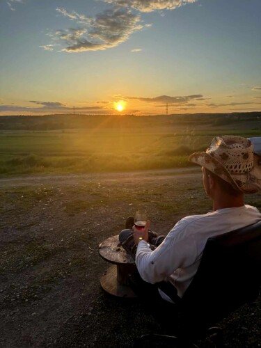 Homme qui regarde un coucher de soleil avec un verre à la main au chalet en location Domaine du ranch Privé en Mauricie, chalet avec spa à Sainte-Ursule