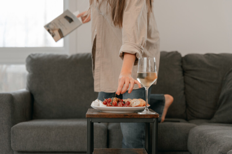 Femme qui pige dans une assiette adossé a un verre de vin dans le salon du chalet en location Le Mëlyā en Estrie, chalet avec foyer au bois à Weedon.