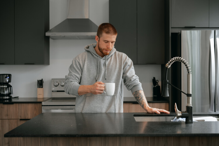 Homme qui regarde sa tassé à café dans la cuisine du chalet à louer Le Mëlyā en Estrie, chalet avec foyer au bois à Weedon.