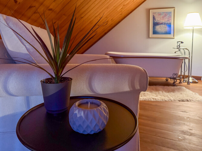 Plante artificielle, chandelle et fauteuil devant une baignoire du Chalet en location Saïra à Lanaudière, chalet avec spa et sauna à Notre-Dame-de-la-Merci.
