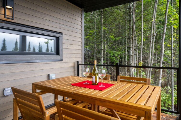 Bouteille de vin blanc et 2 coupes sur la table extérieure du Chalet en location Le Skieur Adstock à Chaudière-Appalaches, chalet avec sauna à Adstock.