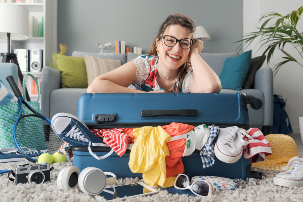 Femme souriante qui s’appuie sur une valise qui déborde de vêtements et accessoires pour un séjour au chalet.